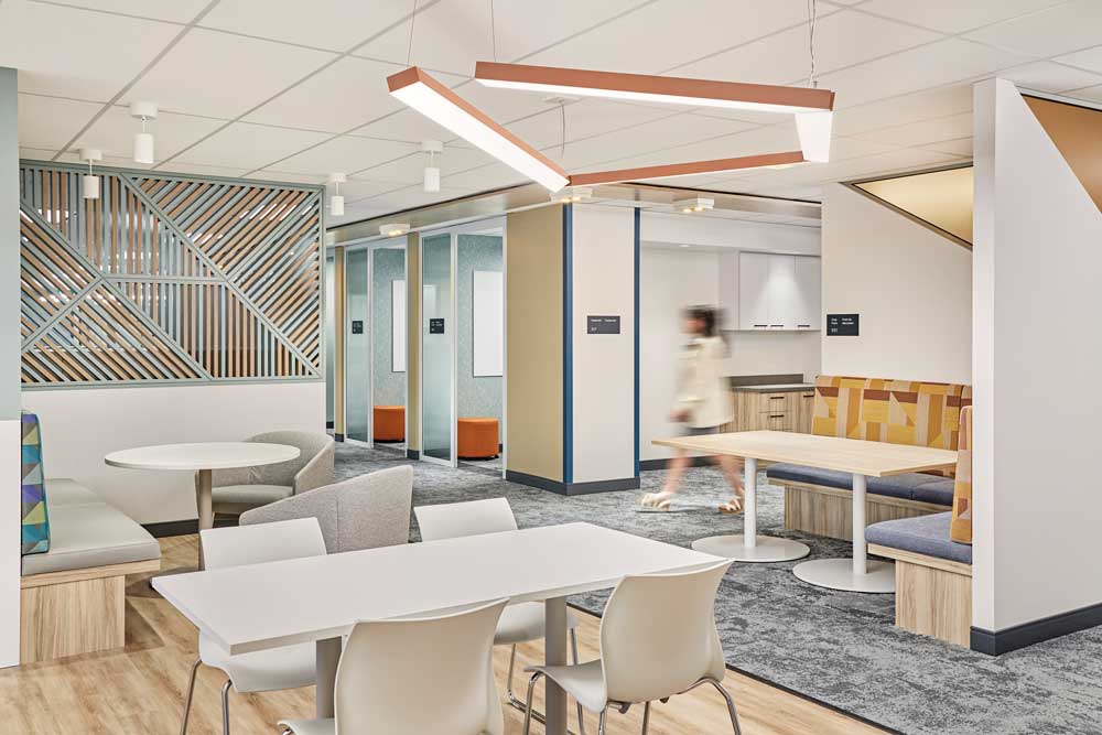 Open collaborative area with tables and benches with geometric lighting above