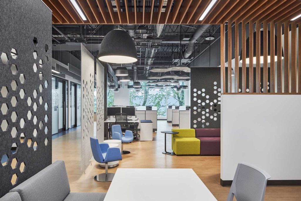 Interior office view with pale wood flooring, mustard and maroon seating with patterned felt acoustical wall dividers.