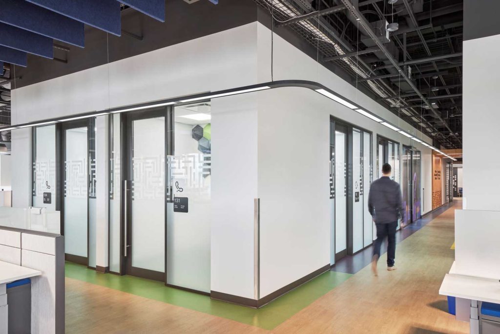A man walks around a corner of interior meeting rooms with full length windows emblazoned with patterned transparent film.