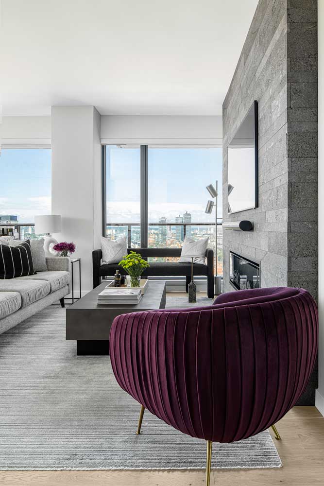 Modern monochromatic furniture and a burgundy accent lounge chair placed around the fireplace in the living room looking over the city