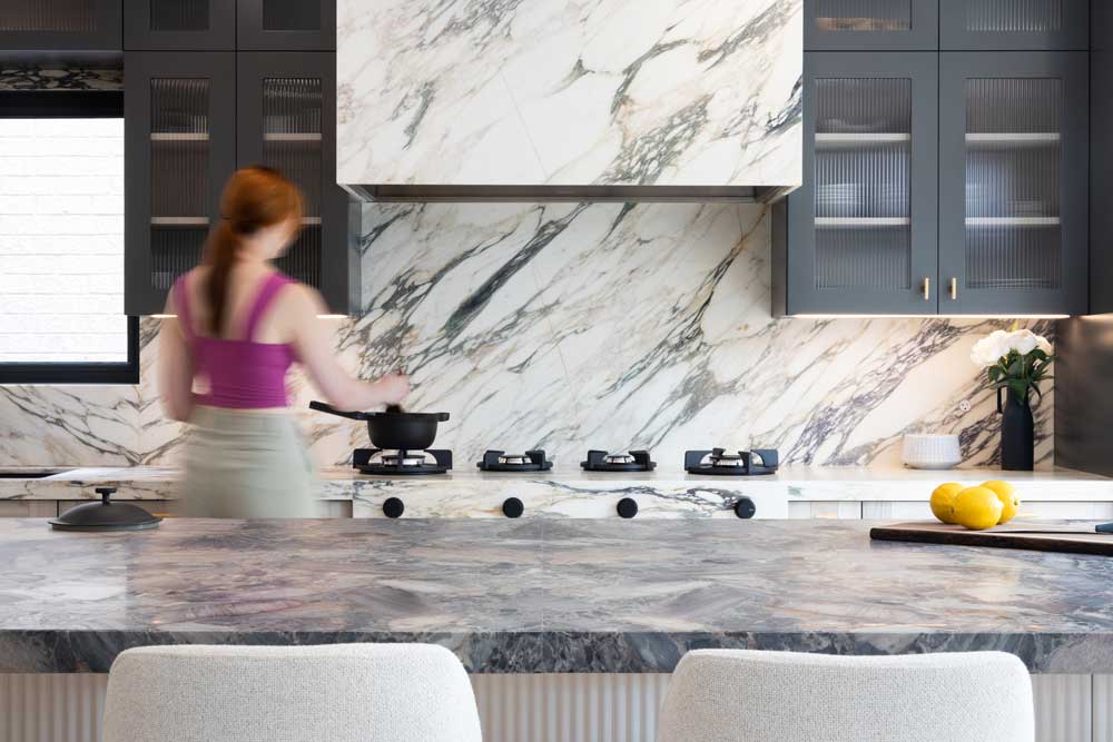 Kitchen countertops and backsplash are covered in luxurious marble with black upper cabinets on both sides of the range hood which is also covered in marble