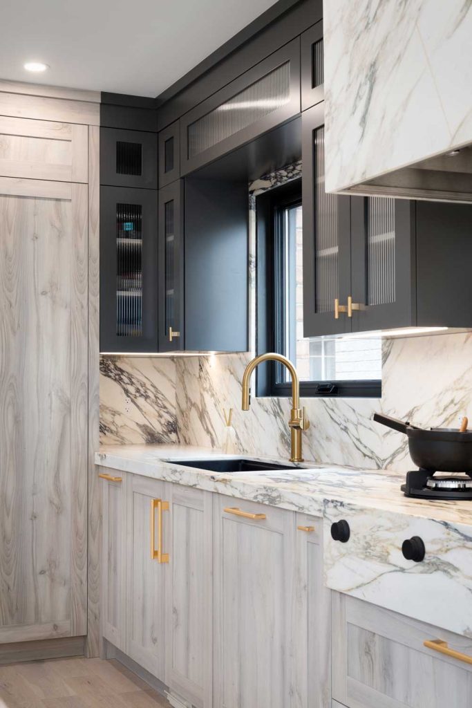 Kitchen countertops and backsplash are covered in luxurious marble with black upper cabinets and light wood finish on the bottom cabinetry. Gold finish hardware throughout