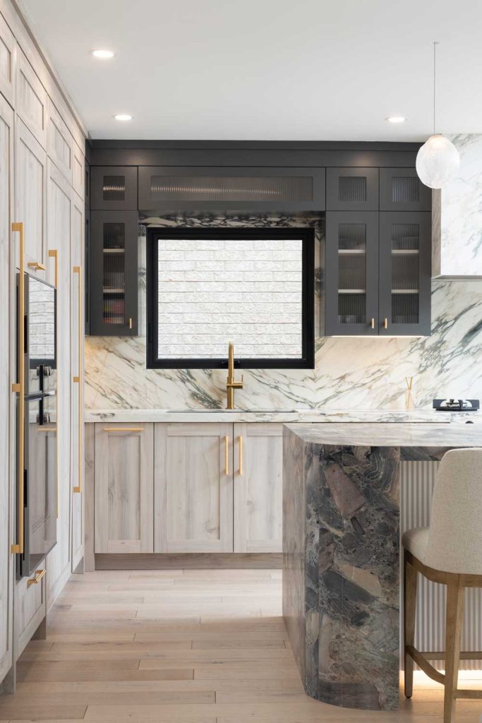 Kitchen countertops and backsplash are covered in luxurious marble with black upper cabinets and light wood finish on the bottom cabinetry. Gold finish hardware throughout