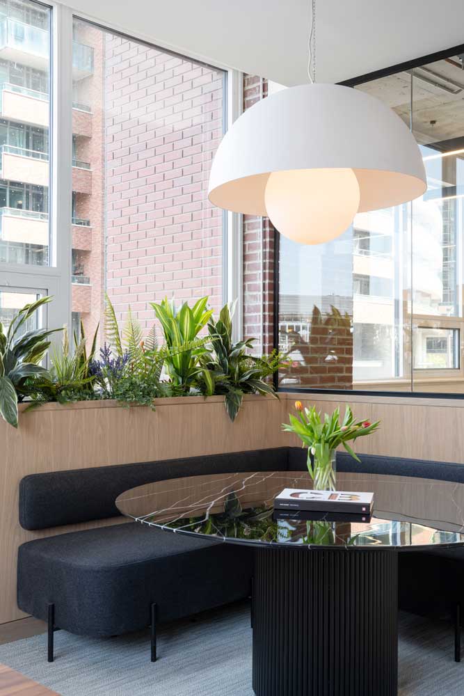 Comfortable and elegant seating and collaboration area showcasing darker toned seating and modern glass top table. Lots of plants and biophilia