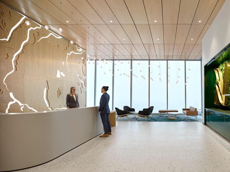 Reception Area at Nutrien, wide open space looking down at the city through a wall of floor to ceiling windows. Behind the reception desk is a design of a map with engraved lit up detail in the wood finish