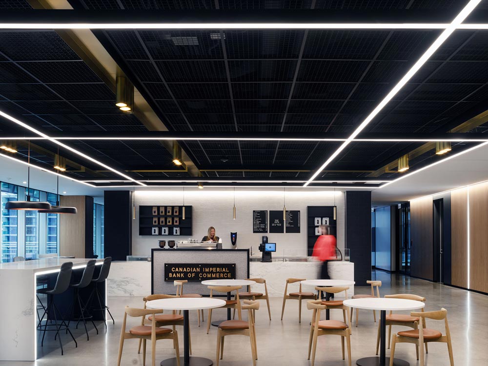 Cafe area with simple modern furniture, linear lighting along the ceiling and same detail on the walls by the elevators 