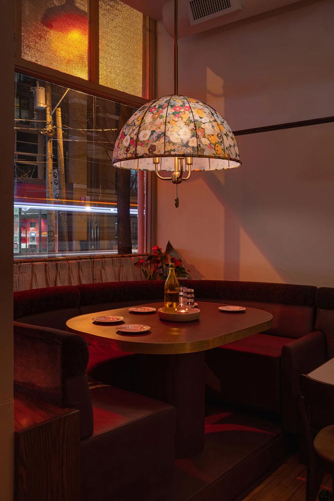 A booth next to the window featuring a a floral pendant light that looks like it belongs in a home of a dear family member