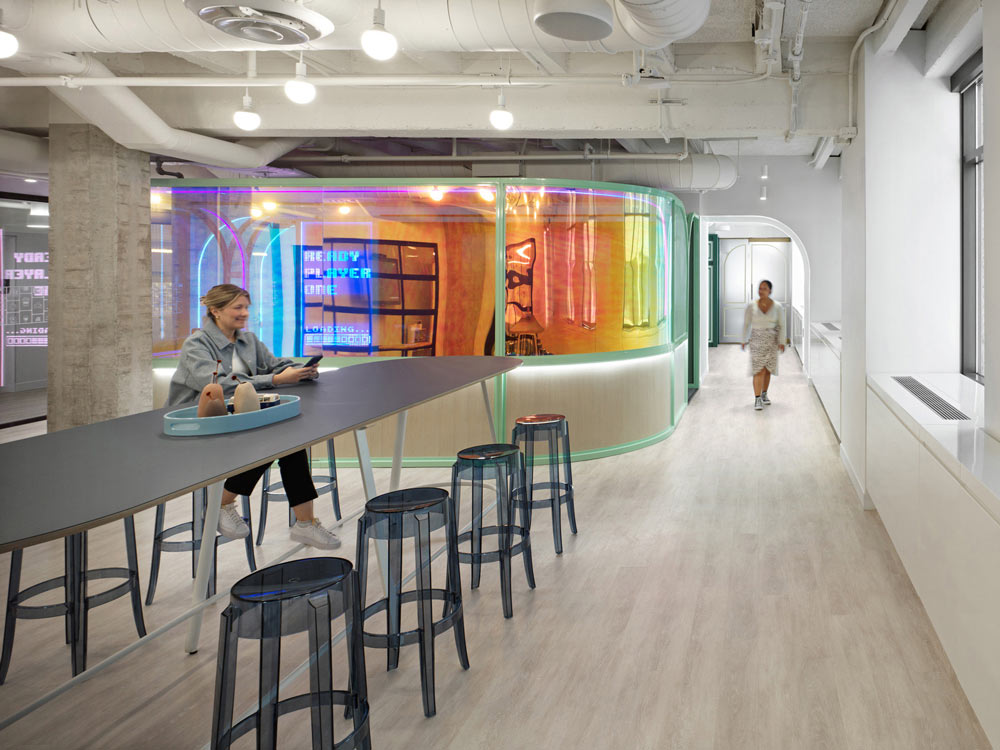 A rainbow coloured glass feature separates this cafeteria and break area in neutral colour palette from another smaller office or lounge space behind the glass