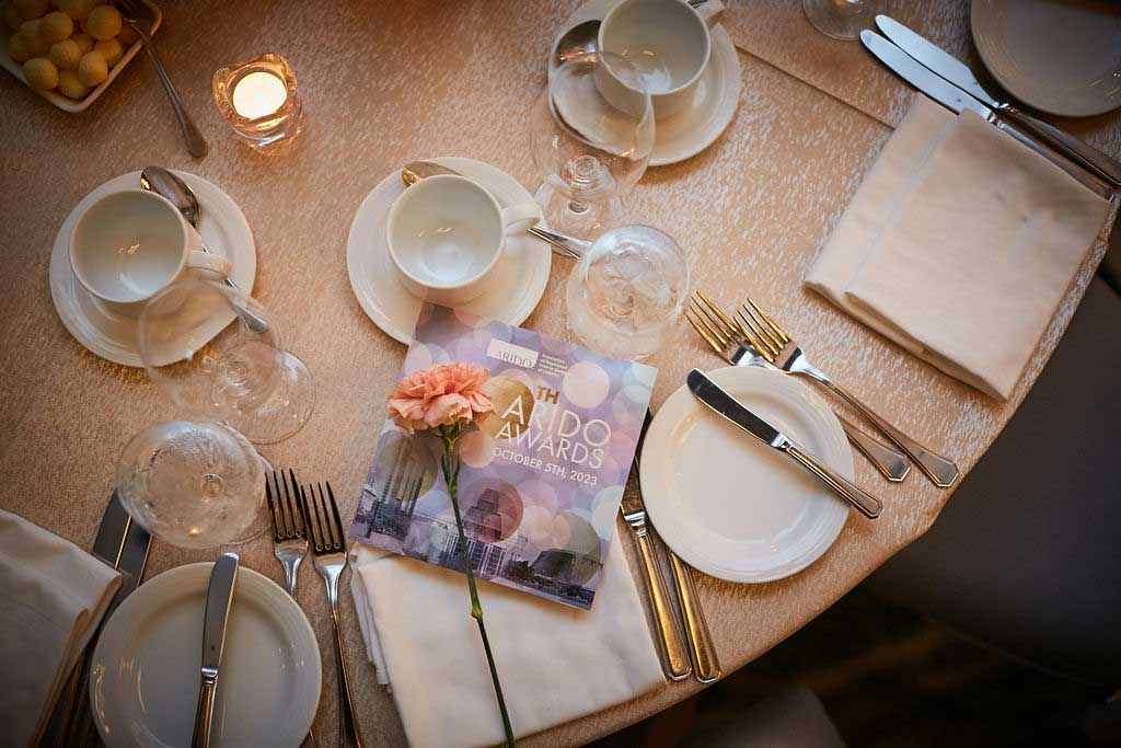 A beautifully set table with the ARIDO Awards table card and a carnation flower.