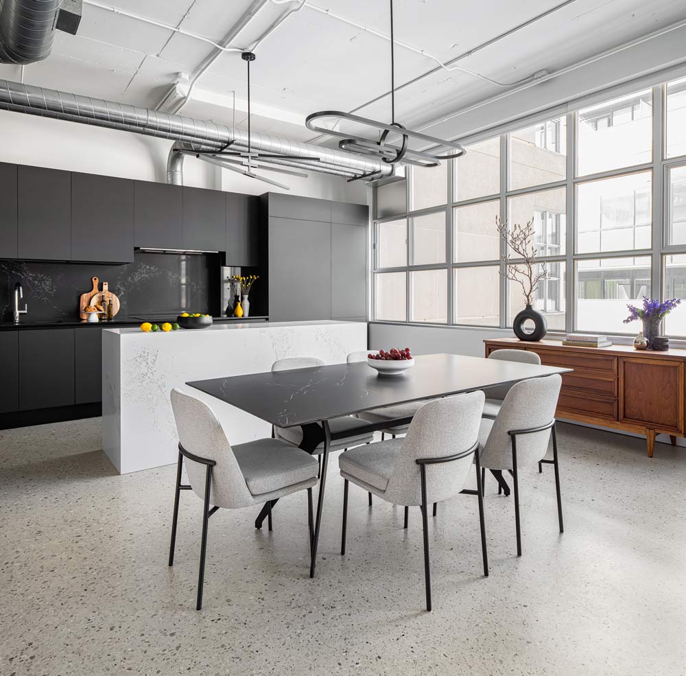 A view of the neutral coloured dining and kitchen areas, looking in the direction of the large windows, and an antique sideboard visible underneath the windows