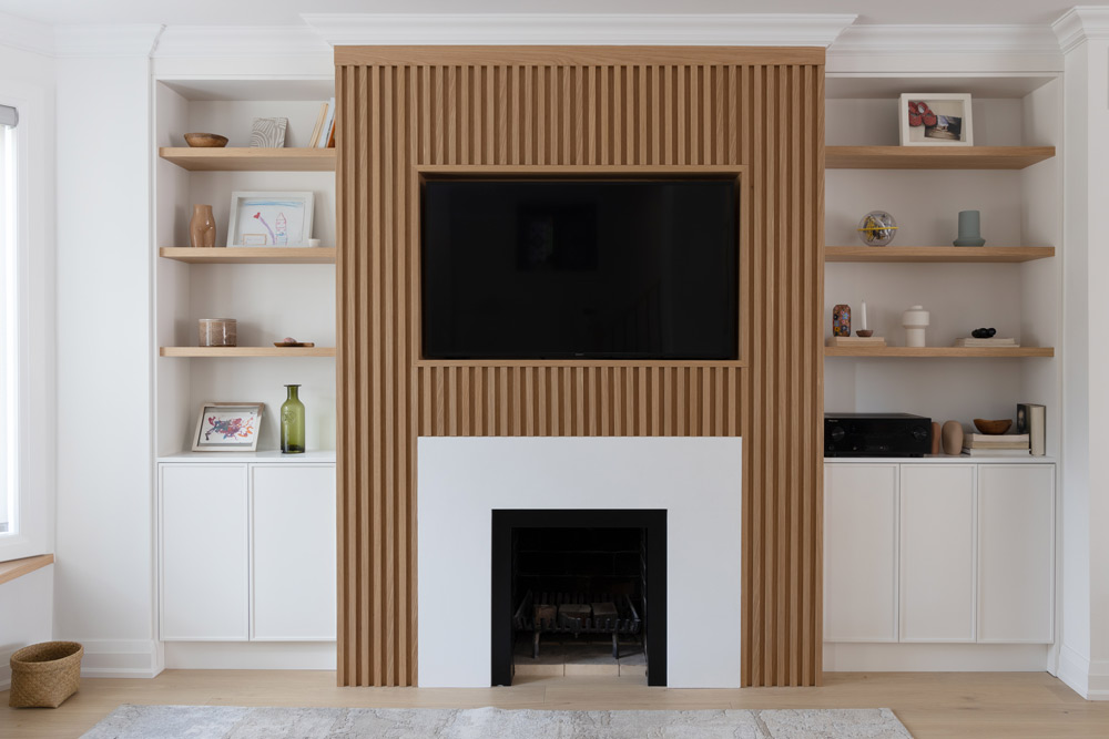 Fire place with the vertical wooden slat detail, and white flat surface encasing the opening of the fire place. Built-in shelving on both sides of the fireplace