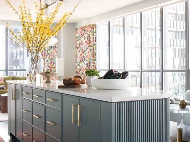 Teal coloured, fluted kitchen island with smooth top counter surface looking onto the living room area and city views out the floor to ceiling windows