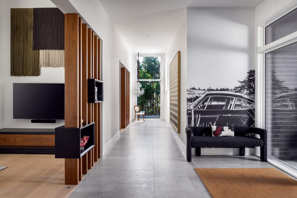 A narrow hallway with walnut slatted partitions on one side and a view of the trees through a narrow floor to ceiling window at the end of the hallway