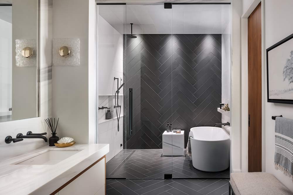 Main bathroom with a white vanity against a dark grey herringbone tile running on the floor and up the shower wall inside the glass shower partition.
