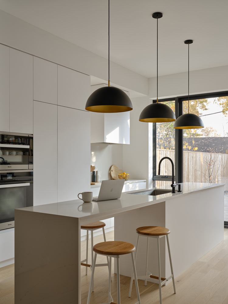 White modern kitchen in all white cabinetry , long island and minimalistic black pendant lights above it