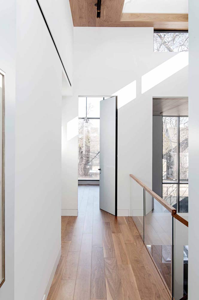 Hallway on the upper floor with glass railings, crisp white walls and wood detailing along the bulkhead above