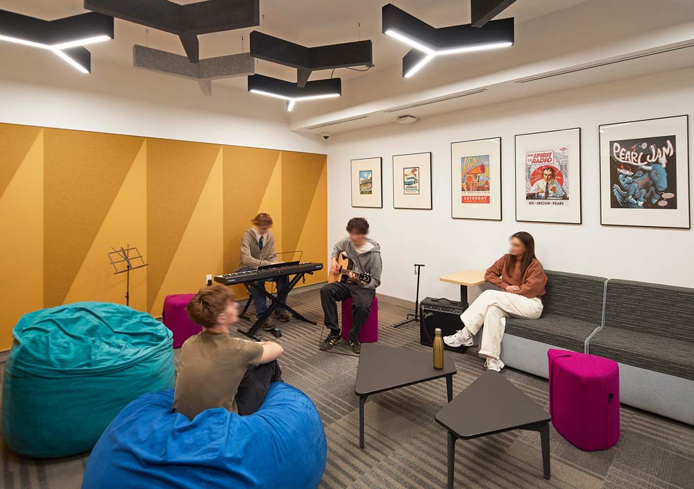 A group of students playing music in the music room with a bright yellow accent wall, and music posters on the other wall, and interesting geometric light fixtures