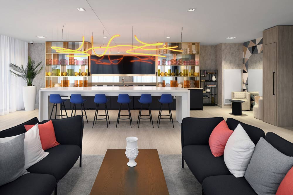 Monochromatic living area and kitchen area with pops of colour of oranges and reds in form of pillows, details on shelves and lively organically shaped light fixture