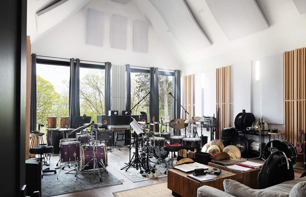 Music room full of music instruments fit for a complete band. The room has pointed high ceilings and tall windows with views of the outdoors