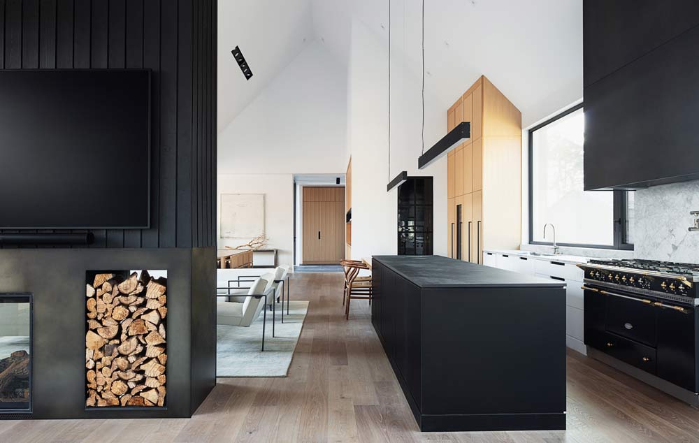 Black kitchen island on the right with a linear black light above, and a fire place on the left, with the living room visible in between