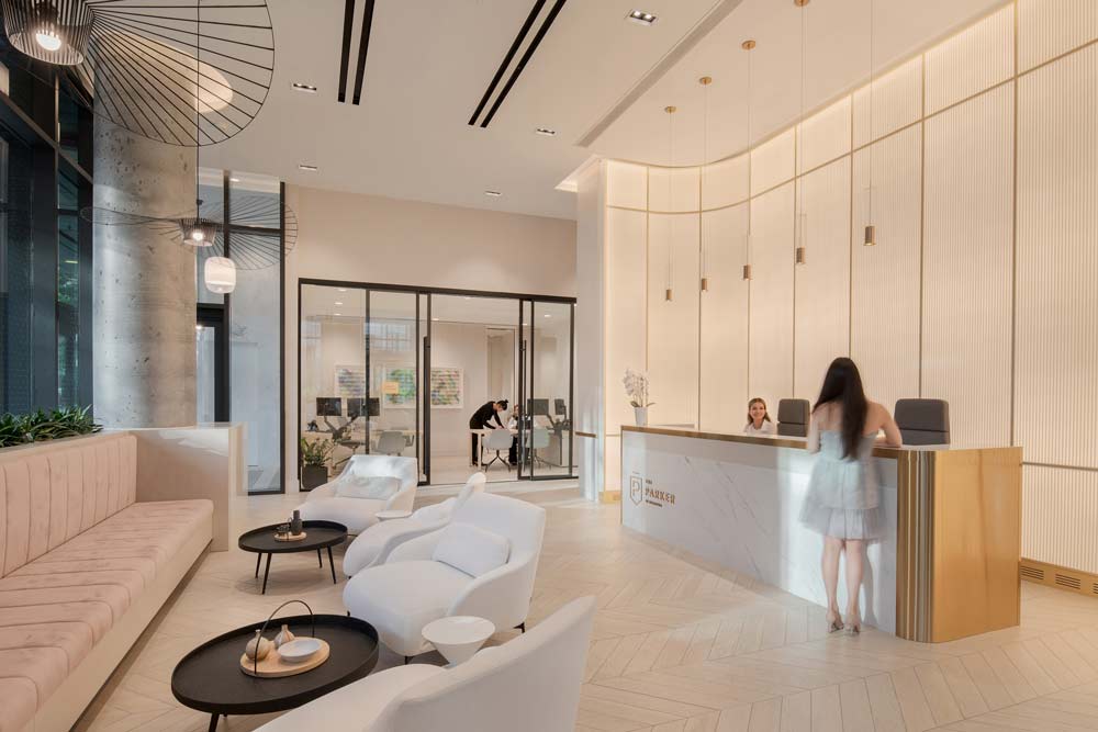 The reception desk and the textured glass wall visible on the right and a small lounge area on the left, tall ceilings. The entire space is designed in light, silvery blond and cream colour scheme