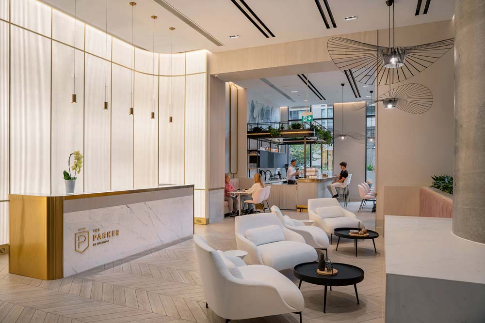A view from the main entrance to the lobby toward the entrance to the 10 Dean cafe, with the reception desk and the textured glass wall visible on the left and a small lounge area on the right