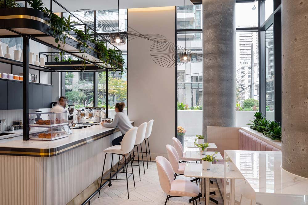 A view of the cafe with the bar on the left and seating booth on the right, the space is filled with cool finishes and biophilic touches