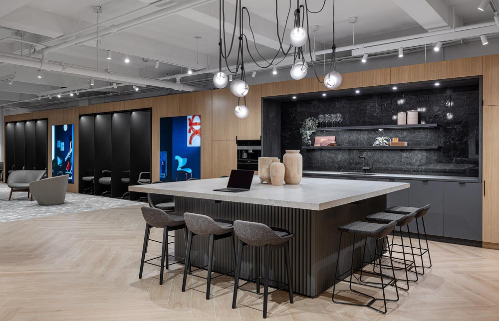 a Kitchen like area in the showroom, with a large square island in the centre, with interesting multi light fixture above, and the furniture displays are visible in the background