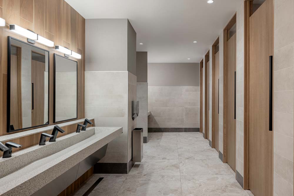 A view of the stalls and sink area across from them. The space is in a calming and welcoming neutral colour pallete and wood finished doors